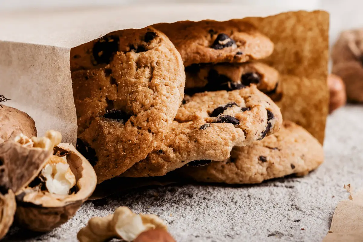 Freshly baked ranger cookies with oats, nuts, and chocolate chips on a wooden table.