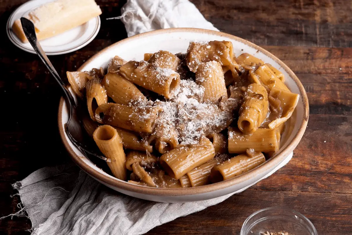 Plated French Onion Pasta with caramelized onions on top, surrounded by fresh ingredients in a rustic kitchen setting.