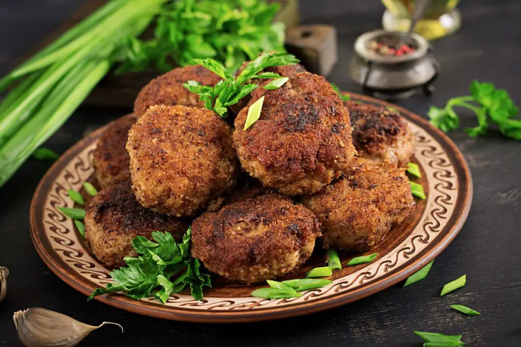 Plate of meatloaf meatballs with parsley garnish and mashed potatoes on a wooden table