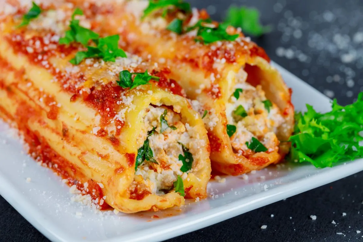 Close-up of a baked manicotti dish garnished with fresh basil on a rustic table.