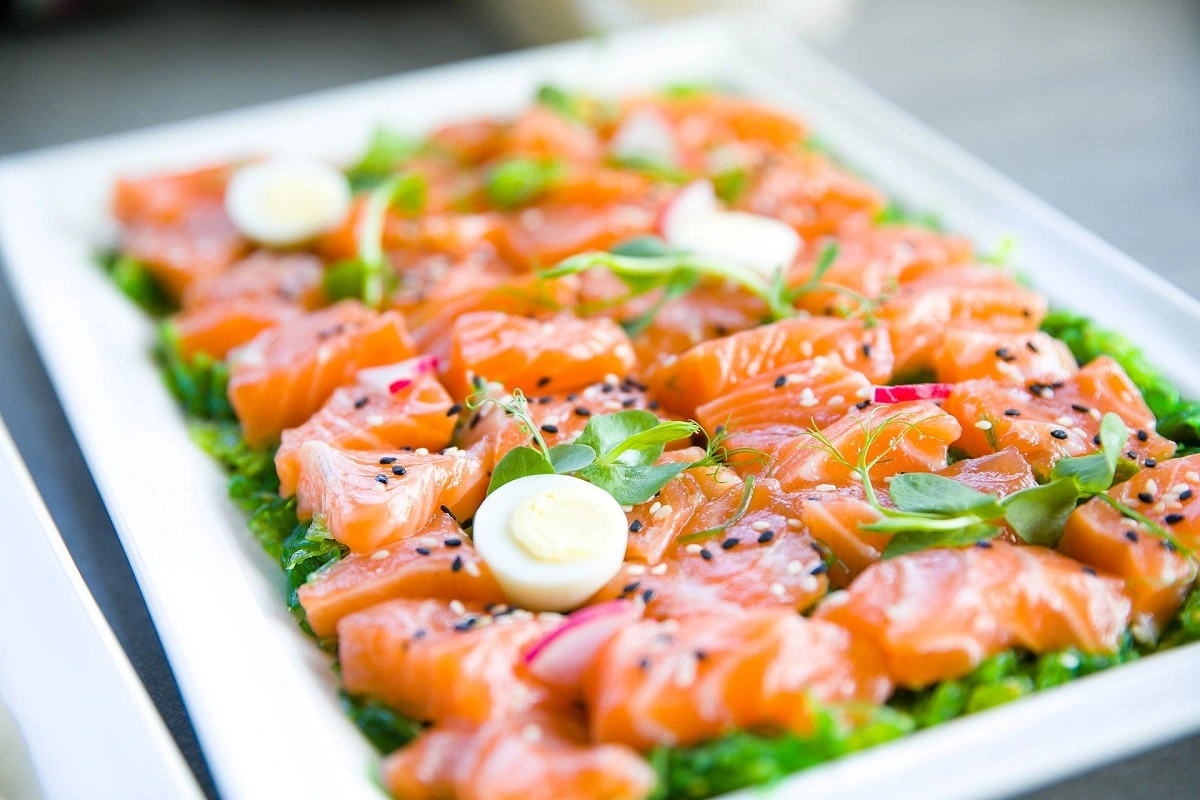 Salmon Crudo on a minimalist plate against a dark background, showcasing the dish's freshness and simplicity.