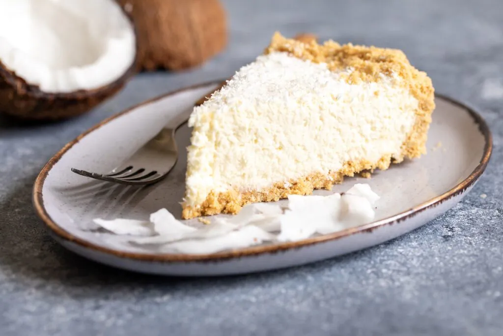 A freshly baked Coconut Custard Pie with golden crust and creamy filling, garnished with coconut flakes on a wooden table